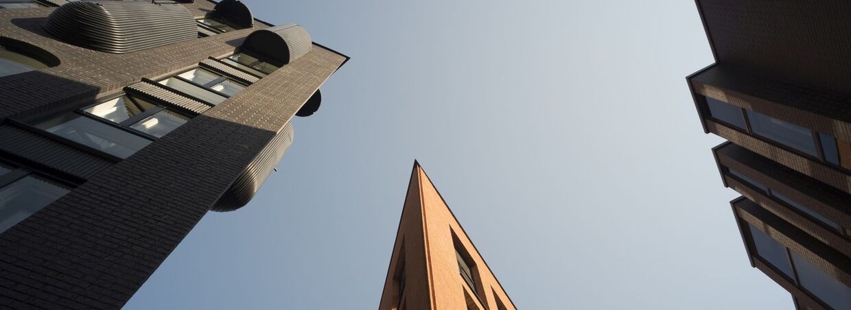 Blick nach oben auf drei moderne Gebäude mit Backsteinfassaden und klarem Himmel.